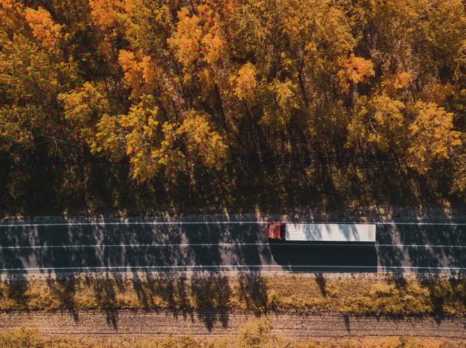 An aerial view of a truck traveling on a road in the fall.