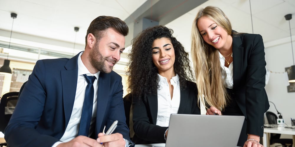 Group dressed in business professional attire surrounding a laptop computer