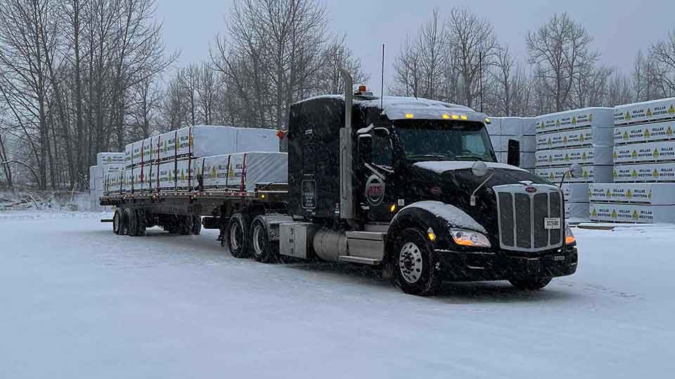 A flatbed truck with a tarped load in winter