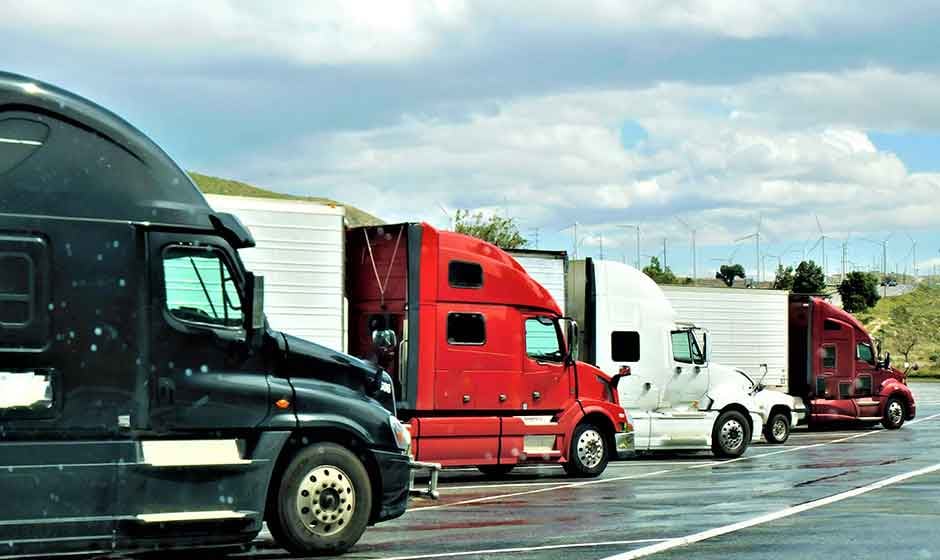 A row of semi trucks parked near a wind farm