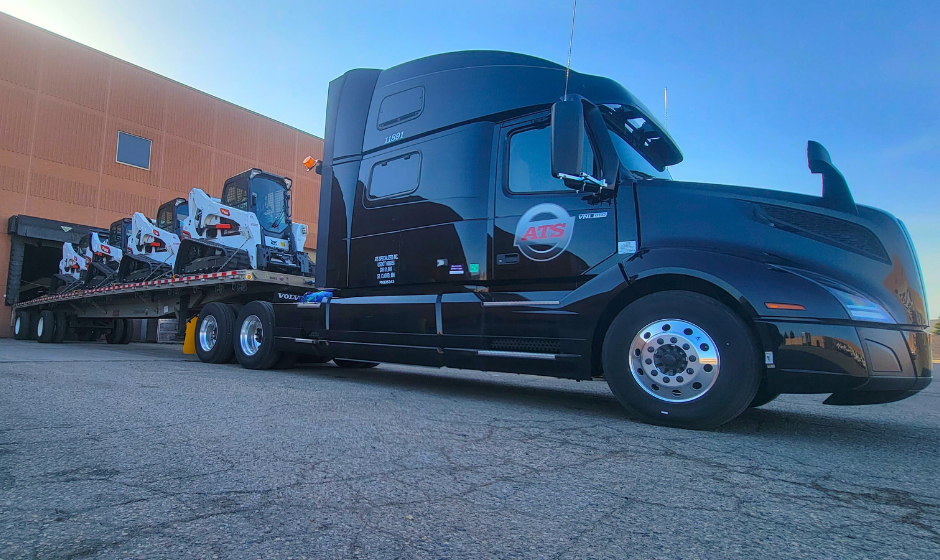 An ATS flatbed truck carries heavy equipment.