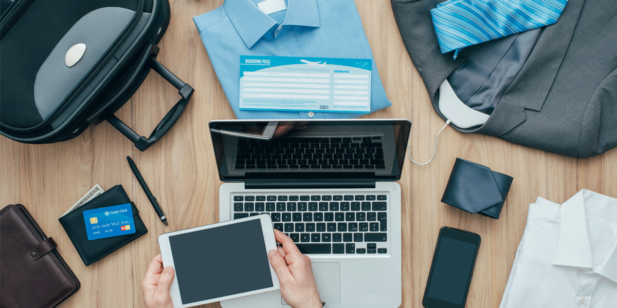 Business trip planning flat lay concept. There's a men's business shirt, a boarding pass, company credit card, luggage, laptop and other technology.