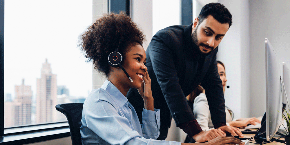 Woman wearing a headset talking to a customer in a call center as a coworker looks on.