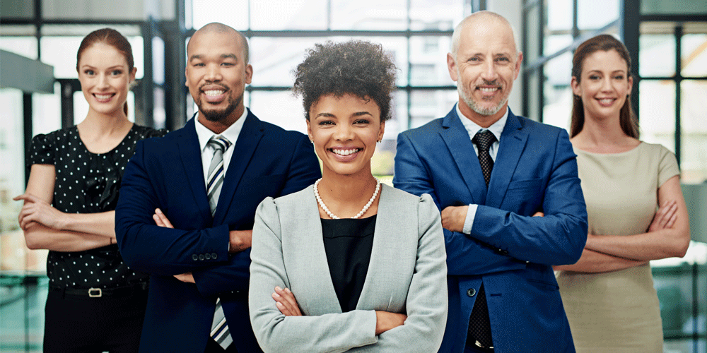 A group of diverse men and women in business clothing smiling at the camera with their arms crossed confidently.