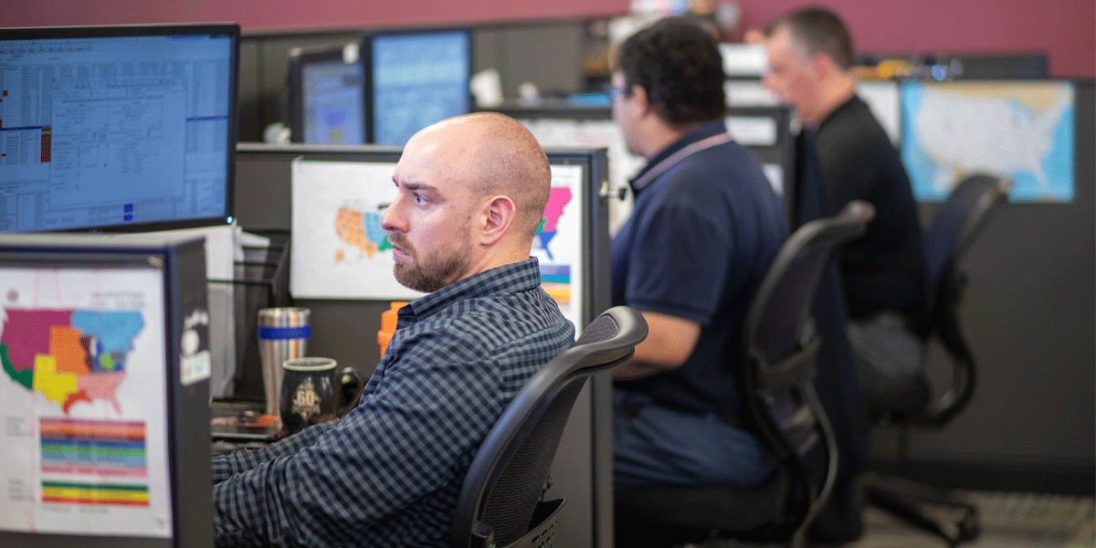 Three men sitting at their desks looking at their computers in a logistics office.