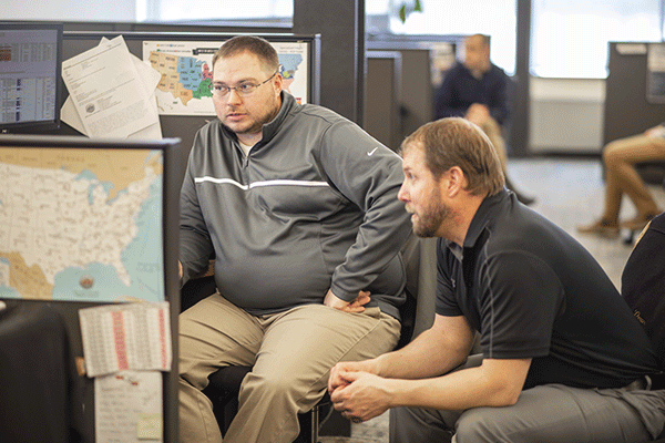 two sales representatives talking at desk