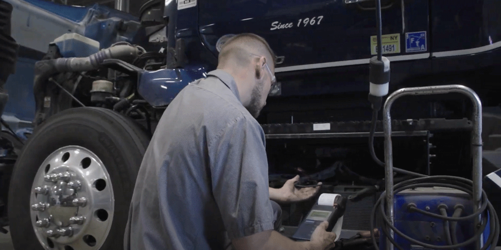 Mechanic kneeling down near the door of a semi-truck looking at a reading.