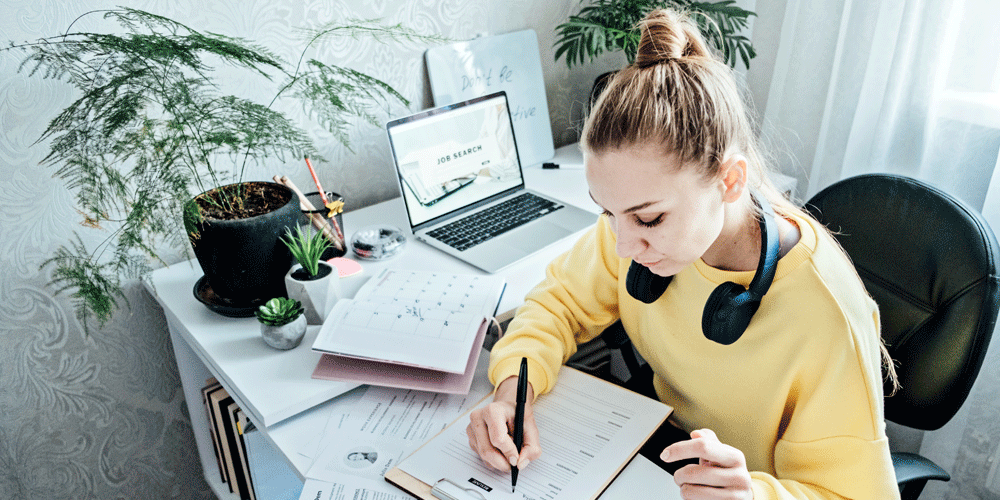 Woman sitting at a desk surrounded by papers as she works on her resume during a job search.